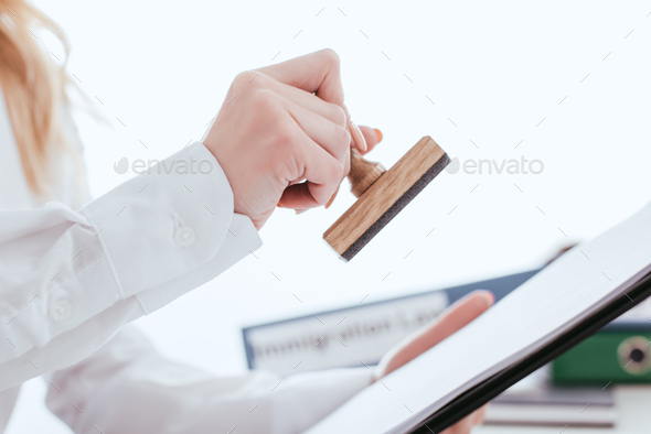 selective focus of female lawyer holding clipboard and stamp in hands isolated on white