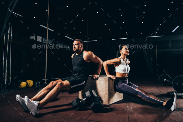 athletic sportsman and sportswoman exercising on cube together in dark gym