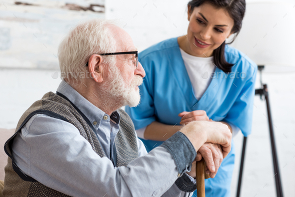 Selective focus of calm gray haired man sitting on couch, near smiling nurse