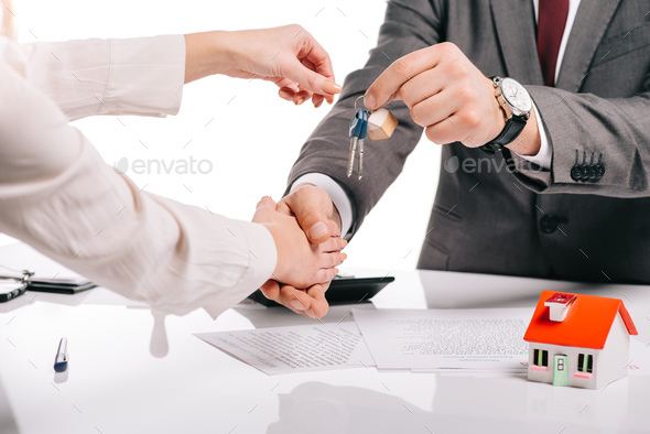 cropped view of mortgage broker shaking hands with woman and holding keys isolated on white,