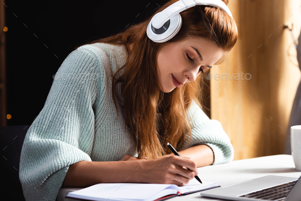 woman in headphones writing and studying online with laptop in cafe