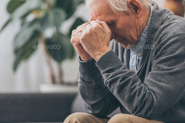 selective focus of upset retired man holding head while sitting on sofa - Stock Photo - Images