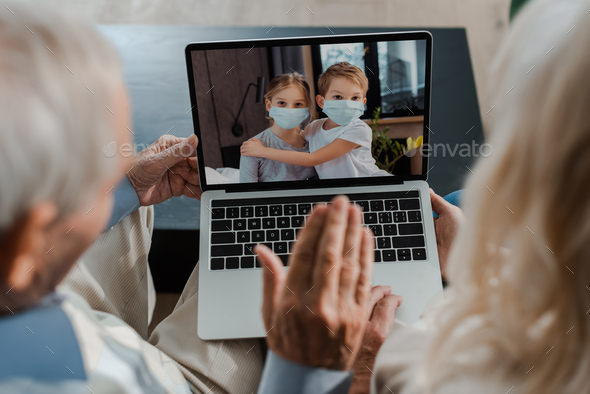 grandparents waving while having video chat with hugging grandchildren in medical masks during self