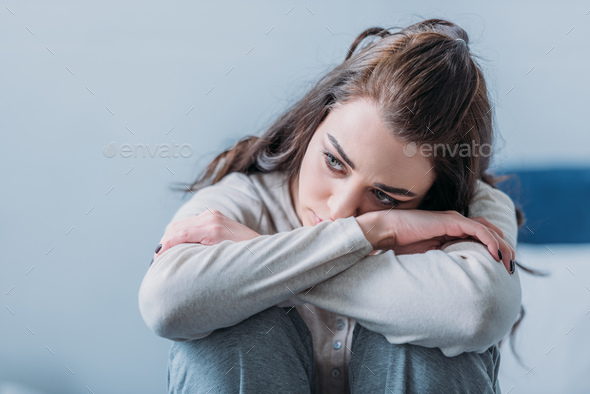 selective focus of beautiful sad woman hugging knees and looking away