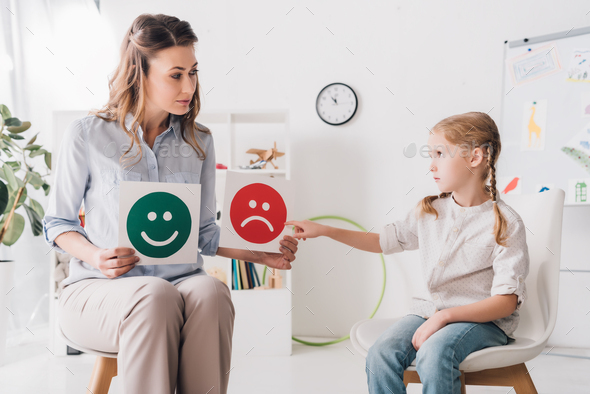 adult psychologist showing happy and sad emotion faces cards to child