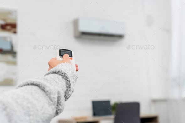 cropped shot of woman in sweater pointing at air conditioner with remote control