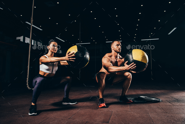 athletic sportsman and sportswoman exercising with medicine balls together in dark gym