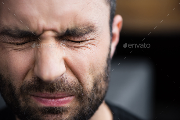 portrait of handsome bearded man crying with closed eyes with tears on face