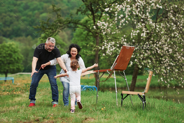 Grandmother and grandfather have fun outdoors with granddaughter. Painting conception