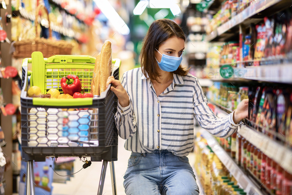 Young woman in medical mask with cart shopping in market