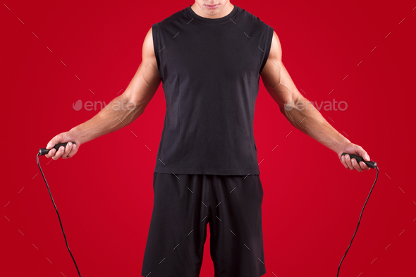 Cardio workout. Cropped view of millennial sportsman jumping on skipping rope on red studio