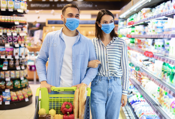 Young couple in protective masks shopping in supermarket
