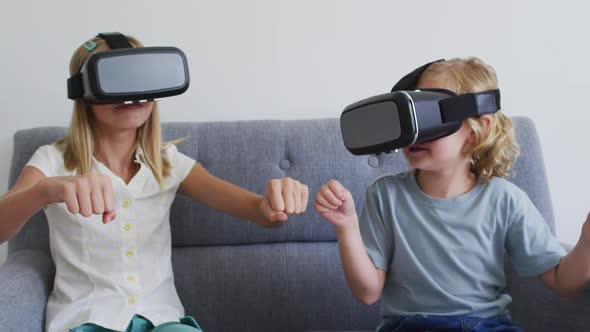 Caucasian brother and sister gesturing while using vr headset sitting on the couch at home alt