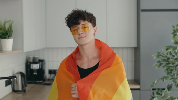 Portrait Shot of Young Stylish Gay Man Wearing Yellow Glasses and Rainbow Flag Over His Shoulder and alt