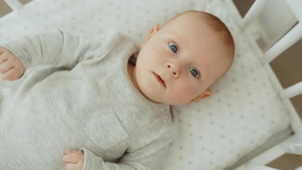 Top View of the Little Newborn Baby Lying on the Cot and Looking at the Camera alt