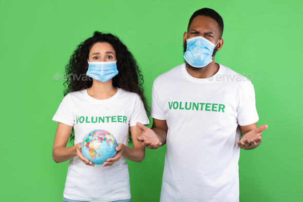 Two Volunteers Holding Globe Wearing Face Masks Over Green Background