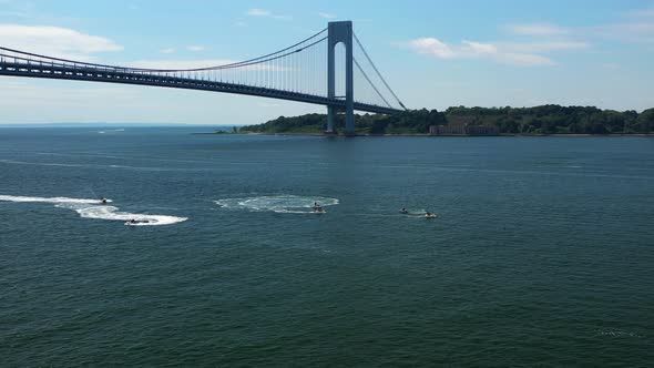 aerial dolly shot forward toward a few jet ski riders circling on the waters below the Verrazano Nar alt