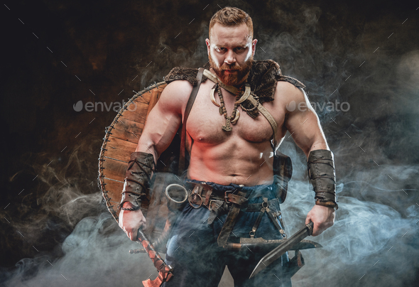 Wild nordic barbarian with hatchet and knife in smokey background