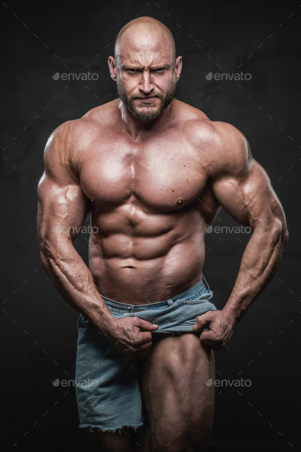 Angry bald bodybuilder pulling his shorts showing his muscular leg ...