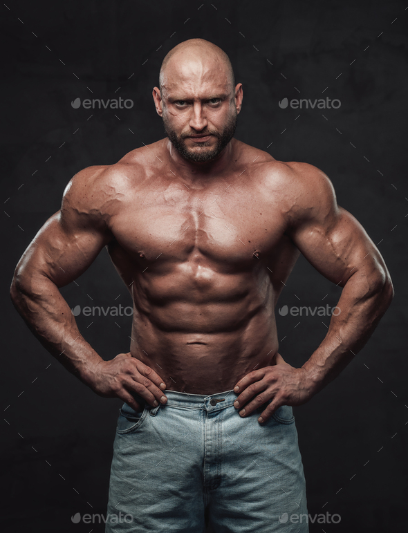 Serious Bald Bodybuilder Posing In Dark Background With Naked Torso