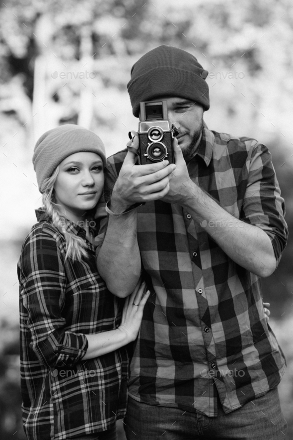 Bald guy with a beard and a blonde girl in bright hats are taking pictures with an old camera