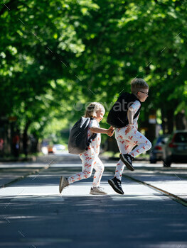 Two children skipping across road with backpacks
