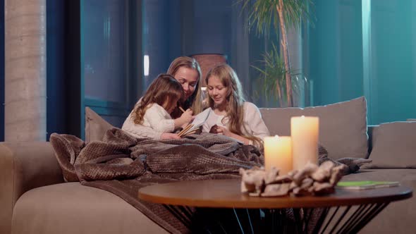 Woman with Daughters Painting in Album While Resting on Sofa alt