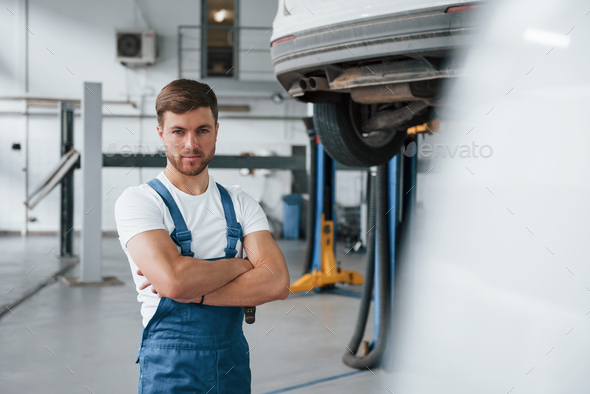 Serious skilled worker. Employee in the blue colored uniform stands in the automobile salon