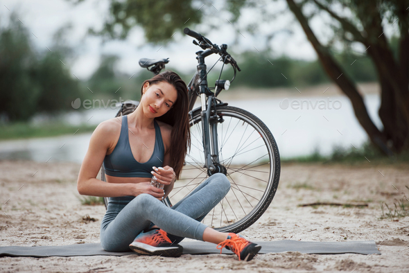 Female cyclist with good body shape sitting near her bike on beach at daytime
