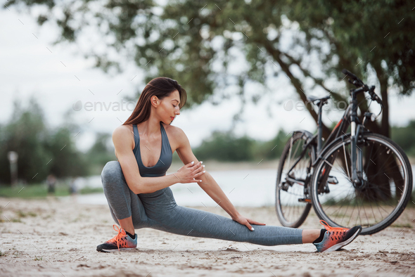 Female cyclist with good body shape doing yoga exercises and stretching