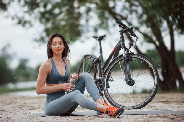 Female cyclist with good body shape sitting near her bike on beach at daytime