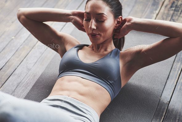 No pain, no results. Girl with slender body works on the abs when lying on the floor