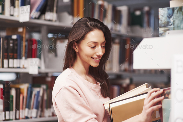 Here you are. Brunette girl in casual clothes having good time in the library full of books