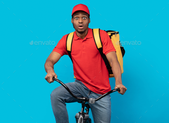Funny amazed black delivery man riding bicycle at studio