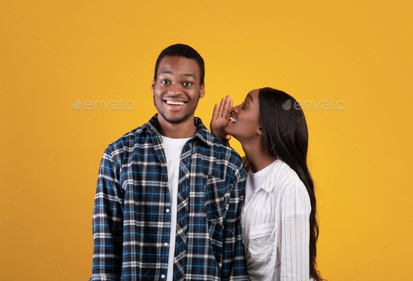Mysterious african american lady in casual whispers in ear of smiling guy