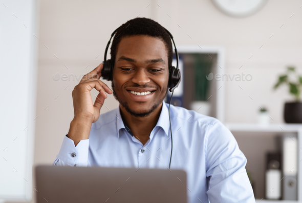 Closeup of black worker with headset using laptop, office interior