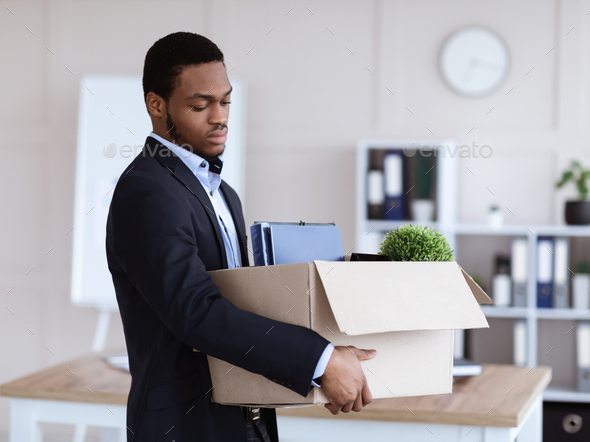 Upset black man got fired, holding box with his belongings