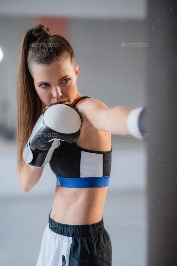 A girl in sports clothes is engaged in boxing and works out a punch with her hand on a punching bag