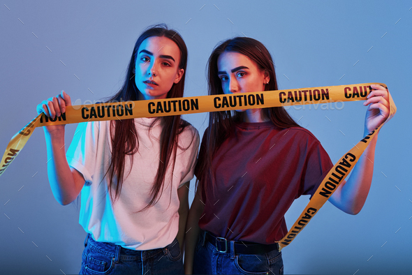 Do not cross this line. Studio shot indoors with neon light. Photo of two beautiful twins