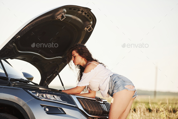 Hot woman open hood of her broken car and fixes it at countryside