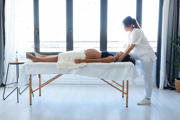Beauty physiotherapist doing osteopathic treatment in pregnant woman's neck on a stretcher at home. - Stock Photo - Images