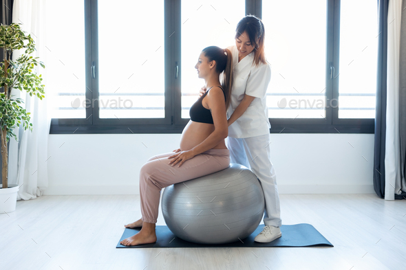 Physiotherapist helping pregnant for doing exercises with ball preparing for childbirth at home. - Stock Photo - Images