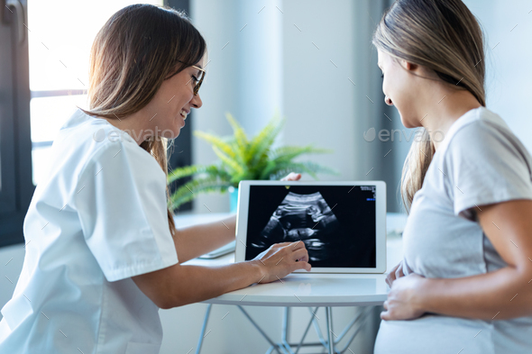 Gynecologist doctor showing to pregnant ultrasound scan baby with digital tablet in consultation. - Stock Photo - Images