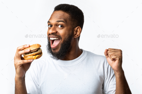 Joyful Black Guy Biting Burger Enjoying Cheat Meal, White Background