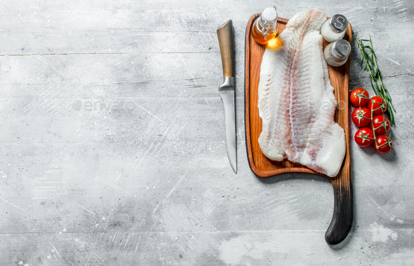 Fish fillet on a cutting Board with a knife, spices, oil and tomatoes on a  branch. Stock Photo by Artem_ka2