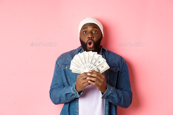 Amazed african-american man receive cash prize, showing money and staring at camera in awe, standing