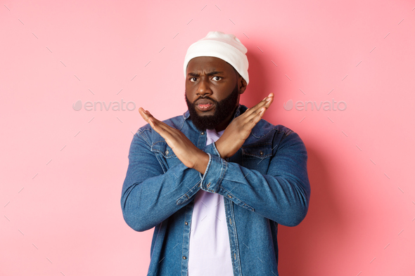 Disappointed Black man, staring at camera displeased and frowning, showing stop cross gesture