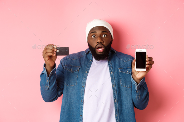 Online shopping. Shocked and concerned Black man staring at camera, showing mobile phone screen and