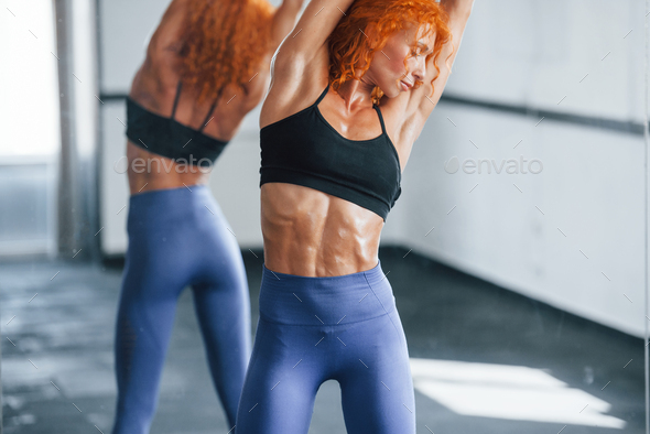 Warm up exercises. Sporty redhead girl have fitness day in gym at daytime.  Muscular body type Stock Photo by mstandret