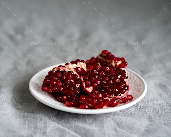 Still life with broken open pomegranate and seeds on plate on table covered with crumpled gray